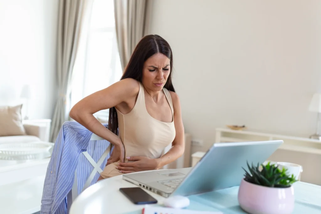 businesswoman holding her back while working laptop home office desk young woman stretching sitting feeling her back tired after working laptop small home office interior